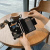 A hand holds a black polka dot passport holder with multi-card slots on a wooden table.