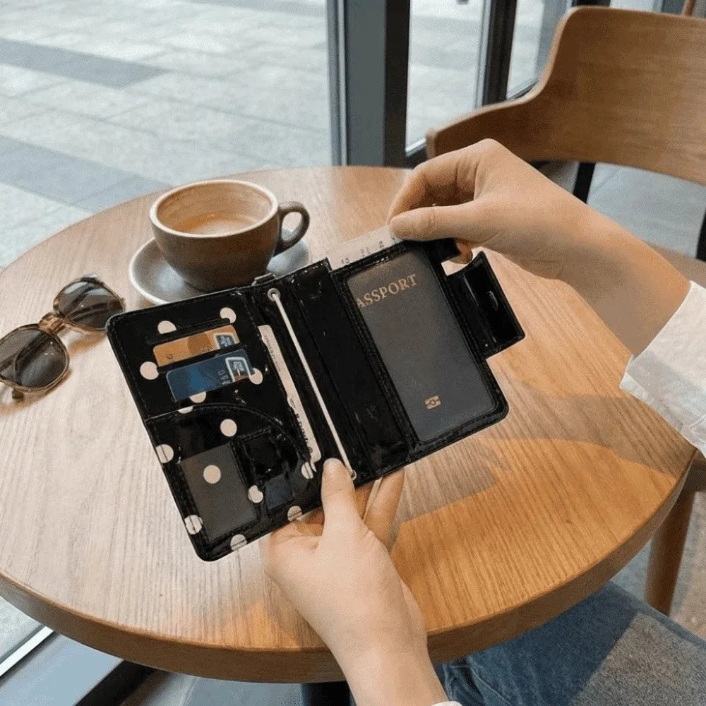 A hand holds a black polka dot passport holder with multi-card slots on a wooden table.