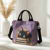 Lila Tasche mit Blumenkattenmuster und schwarzen Riemen auf weißem Untergrund.