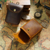 A brown leather multi-functional waist bag is shown open on an aged map background with various antique items.