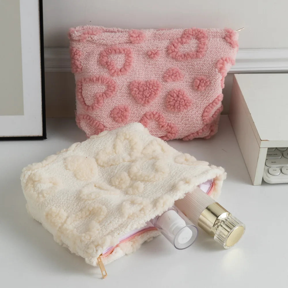 A pink plush heart-pattern storage bag for cosmetics and travel is shown next to a cream-colored version.