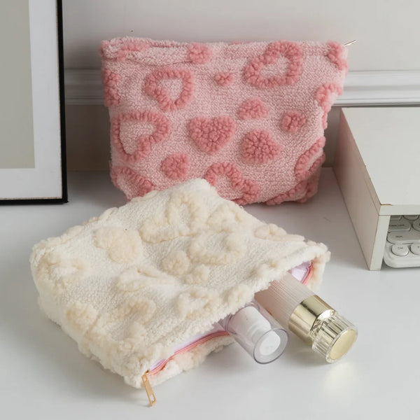 A pink plush heart-pattern storage bag for cosmetics and travel is shown next to a cream-colored version.