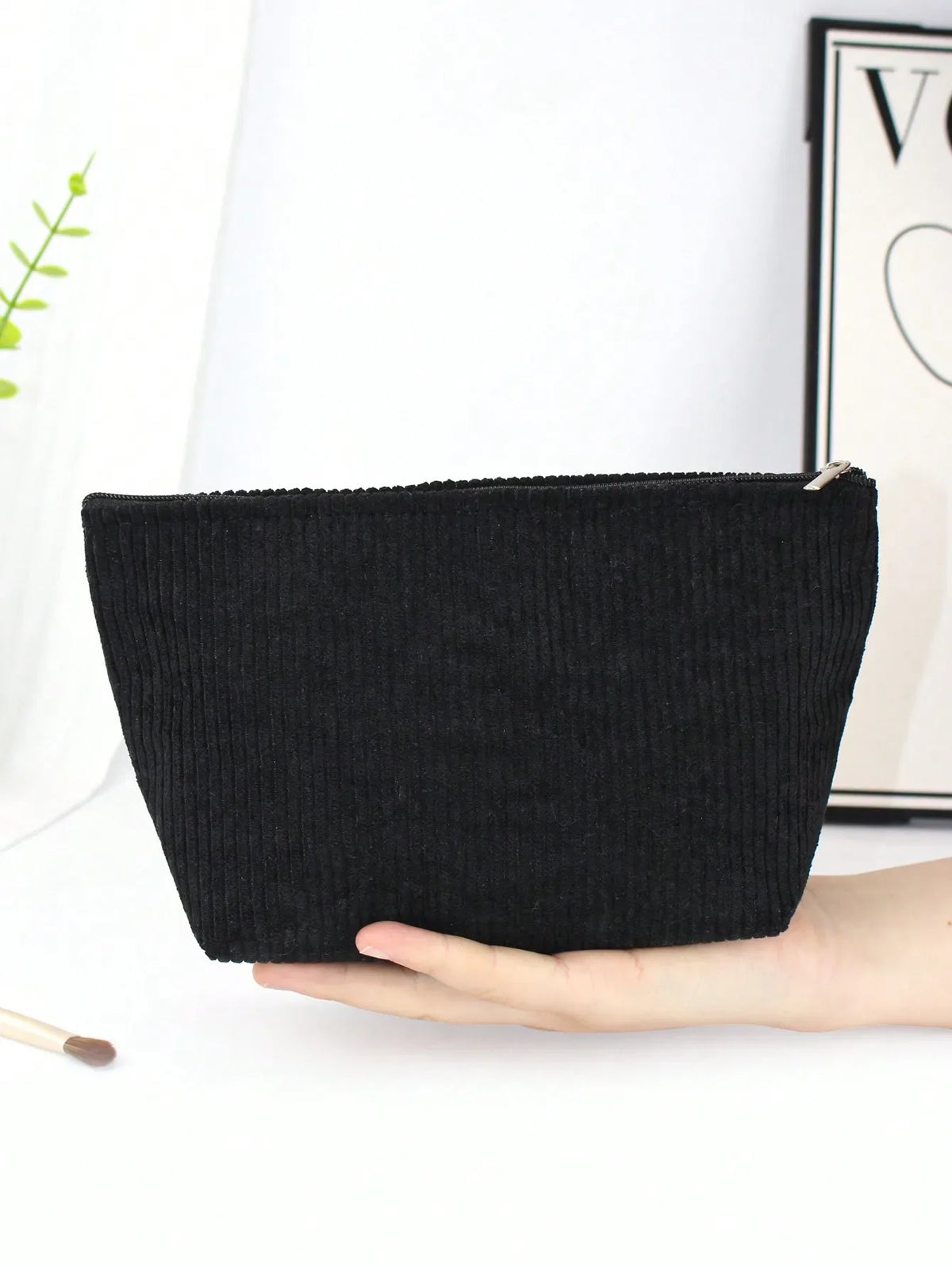 A black corduroy makeup organizer bag with an octagonal design is held in a hand.