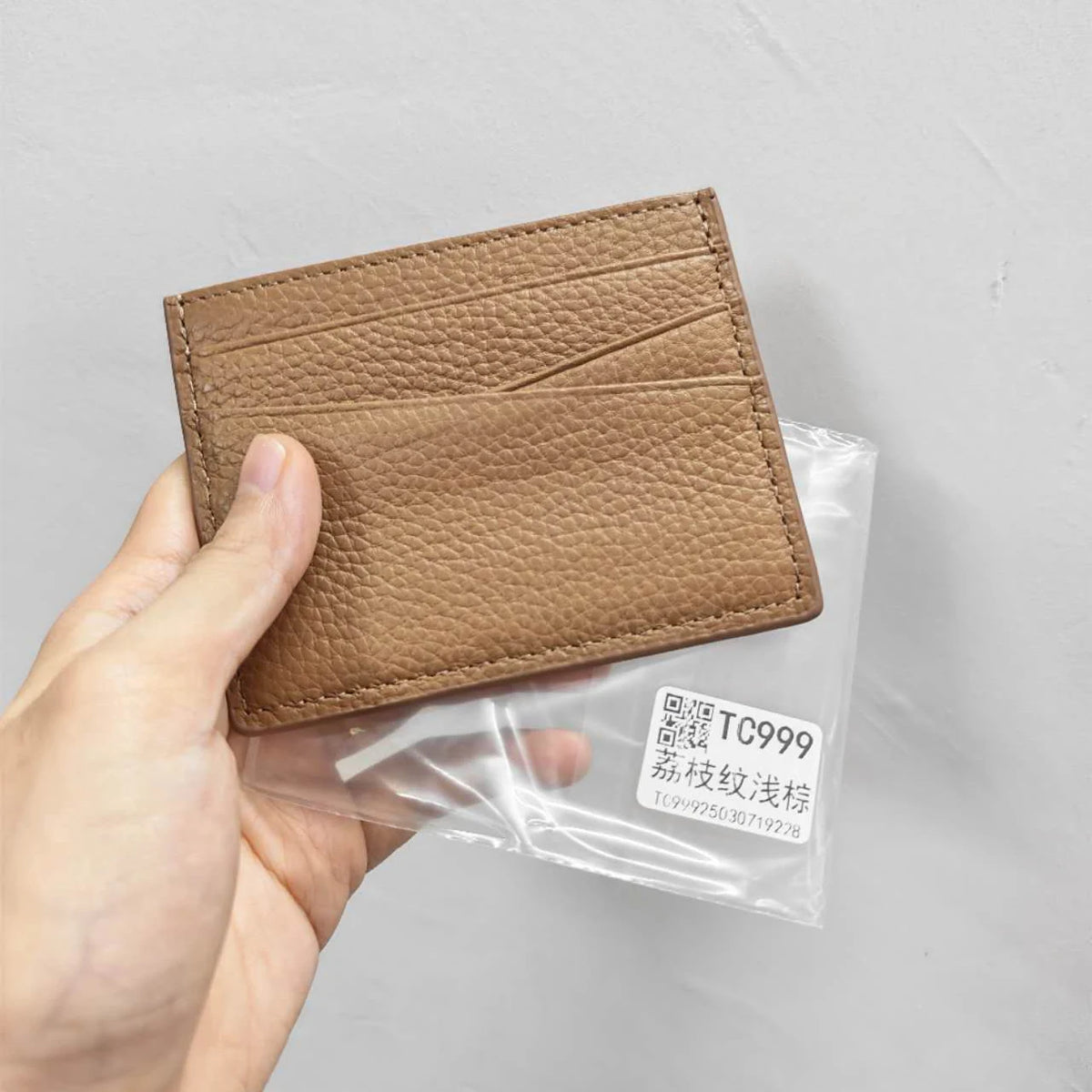 Une main tient un porte-cartes en cuir brun authentique avec une gravure personnalisée à l'intérieur d'une gaine en plastique