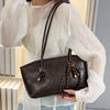 A woman models a brown classic PU leather tote bag with a leather strap and sheer white blouse.