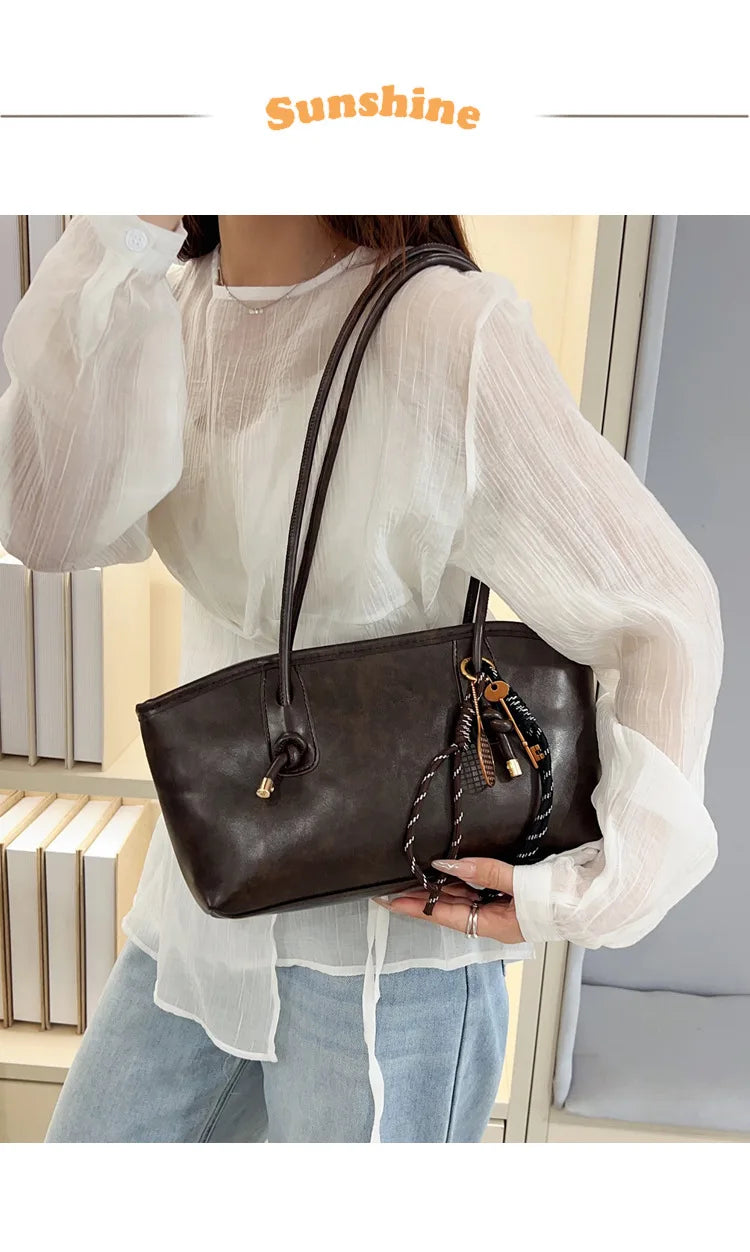 A woman models a brown classic PU leather tote bag with a leather strap and sheer white blouse.