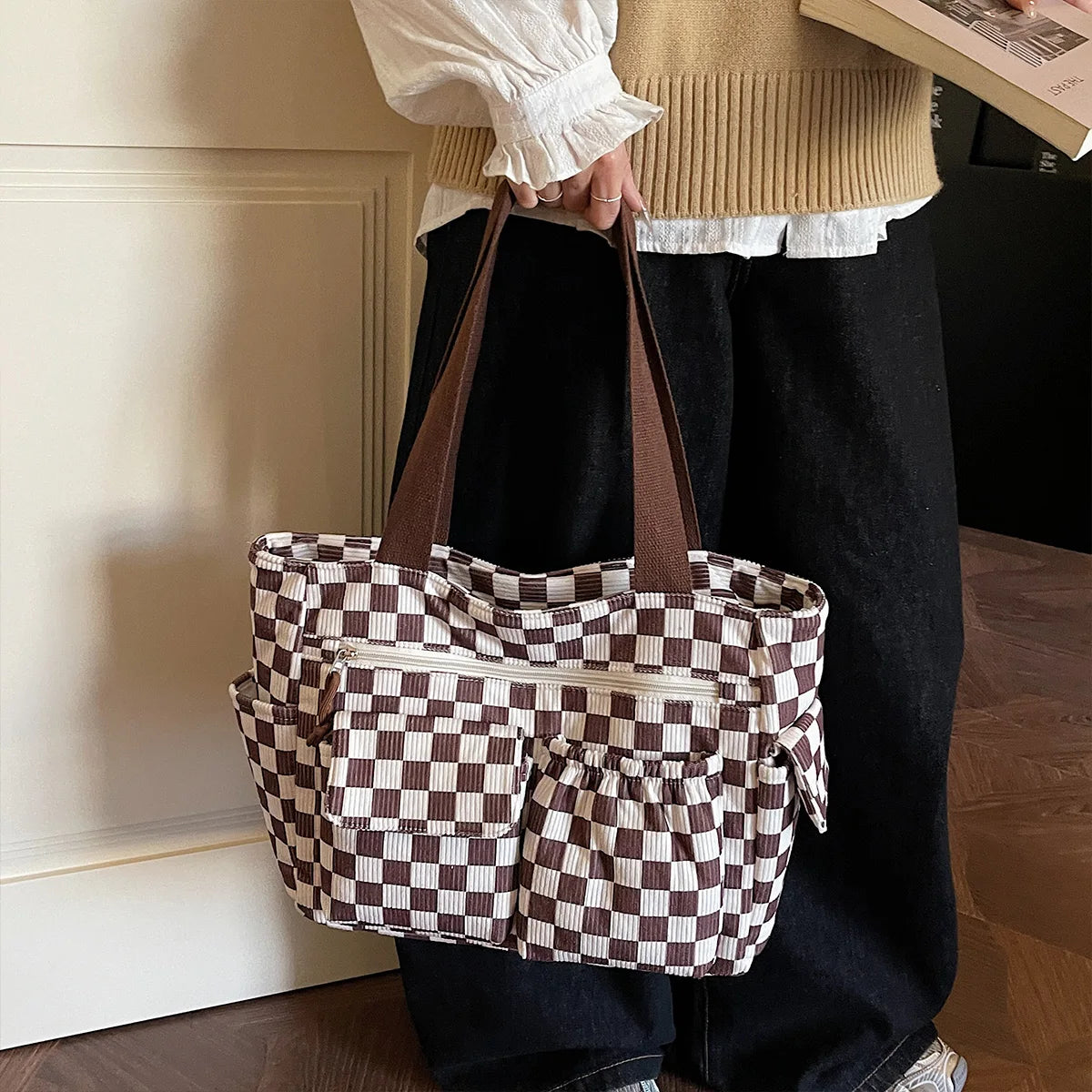 A person holds a brown corduroy tote bag with a checkered pattern against a white door frame.