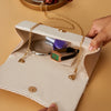 A hand holds a satin evening clutch with a gold chain strap and a purple accessory.