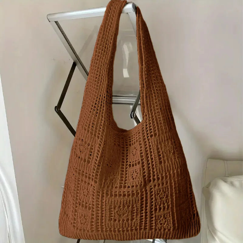 A brown knitted shoulder bag hanging on a silver metal rack.
