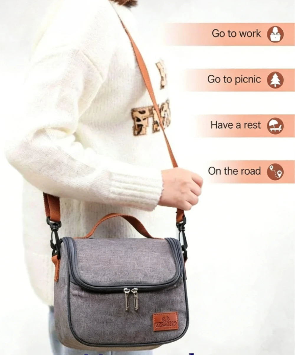 A person wearing a white sweater is carrying a gray insulated reusable lunch bag with a brown strap.