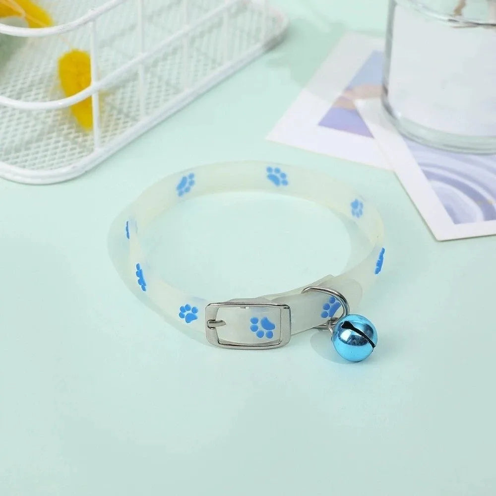 A white glow-in-the-dark pet collar with blue paw prints is displayed on a light green surface.