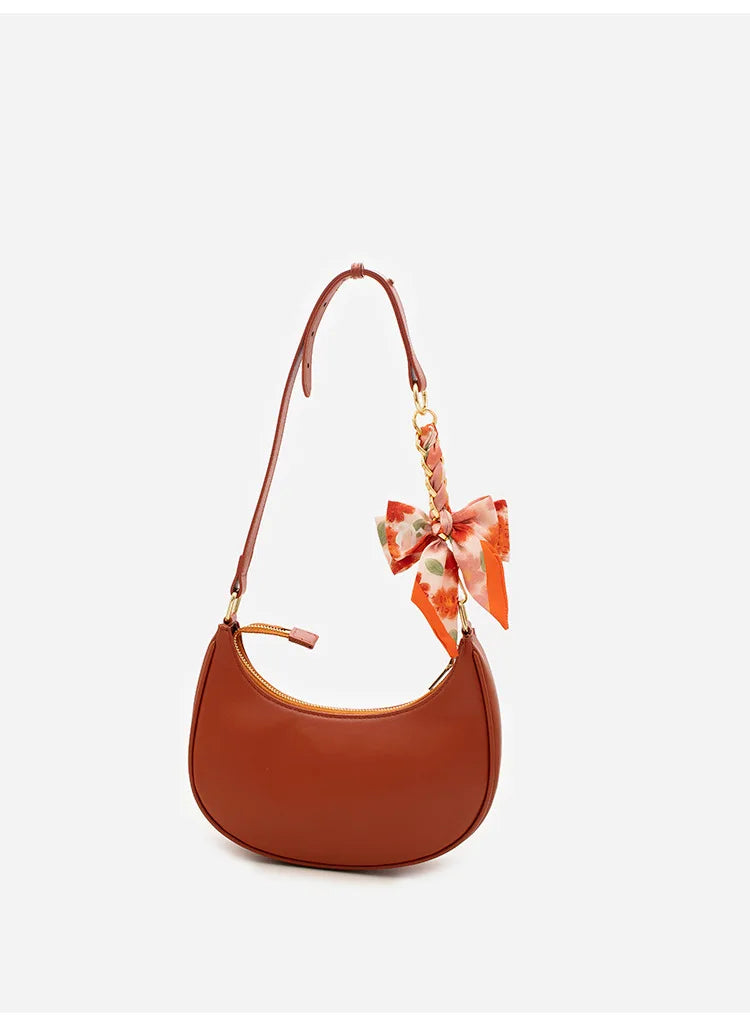 A brown leather bow bag with a chain strap extension and a floral fabric bow detail.