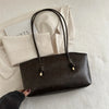 A dark brown PU leather tote bag with black handles resting on a white textured surface.
