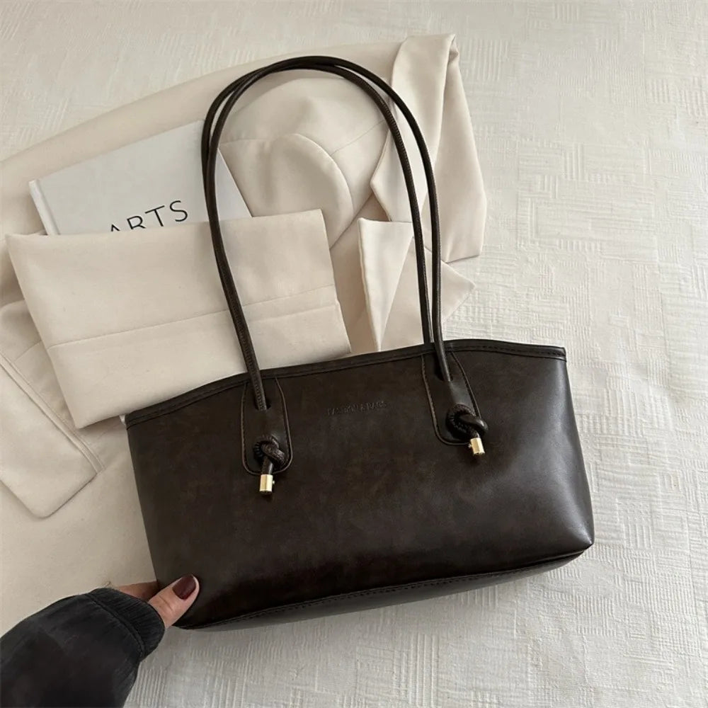 A dark brown PU leather tote bag with black handles resting on a white textured surface.