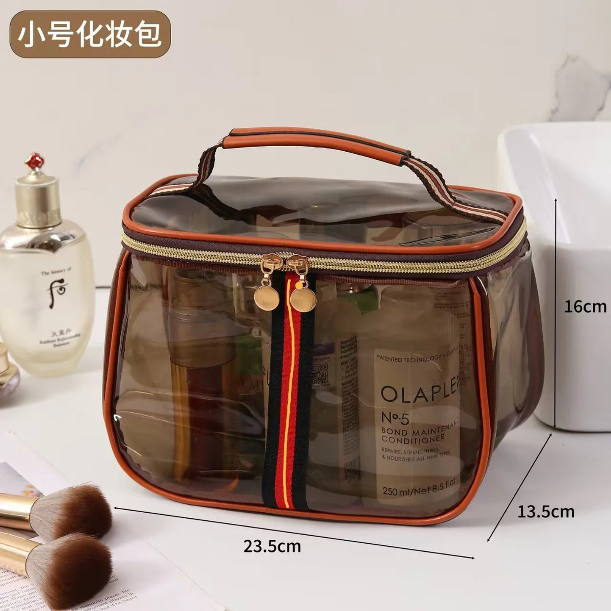 A clear plastic waterproof travel toiletry bag with an orange trim and black stripes, shown next to a bottle of lotion and ma