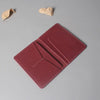 A maroon genuine cowhide leather passport and ticket holder with stitched edges, resting on a gray surface.