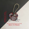 A hand sewn rhinestone beaded bag charm shaped like a crab with a gold string for hanging.