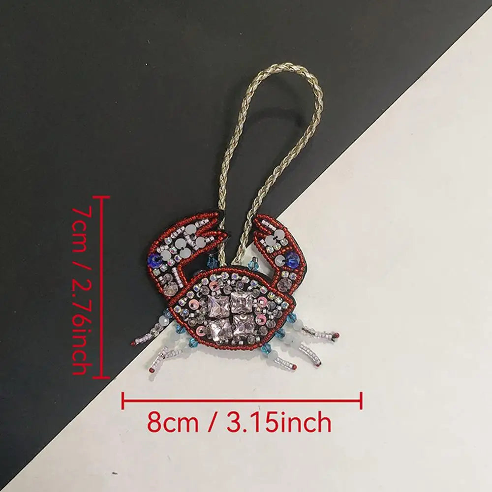 A hand sewn rhinestone beaded bag charm shaped like a crab with a gold string for hanging.