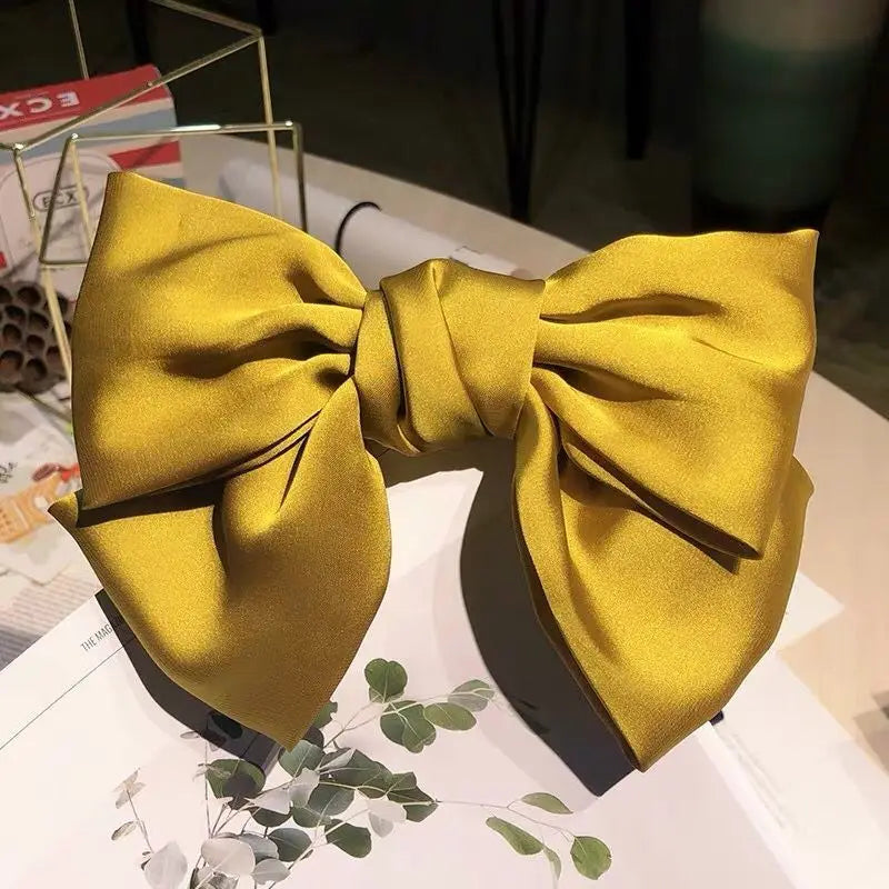 A bright yellow silk bow hair clip tied in a large bow shape.