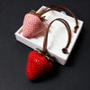 Charm à clés en forme de fraise rose et rouge, présenté dans une boîte rectangulaire blanche.
