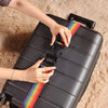 A hand is adjusting a colorful luggage strap on a black rolling suitcase.