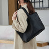 A person is carrying a black handwoven vegan leather tote bag with a textured pattern.
