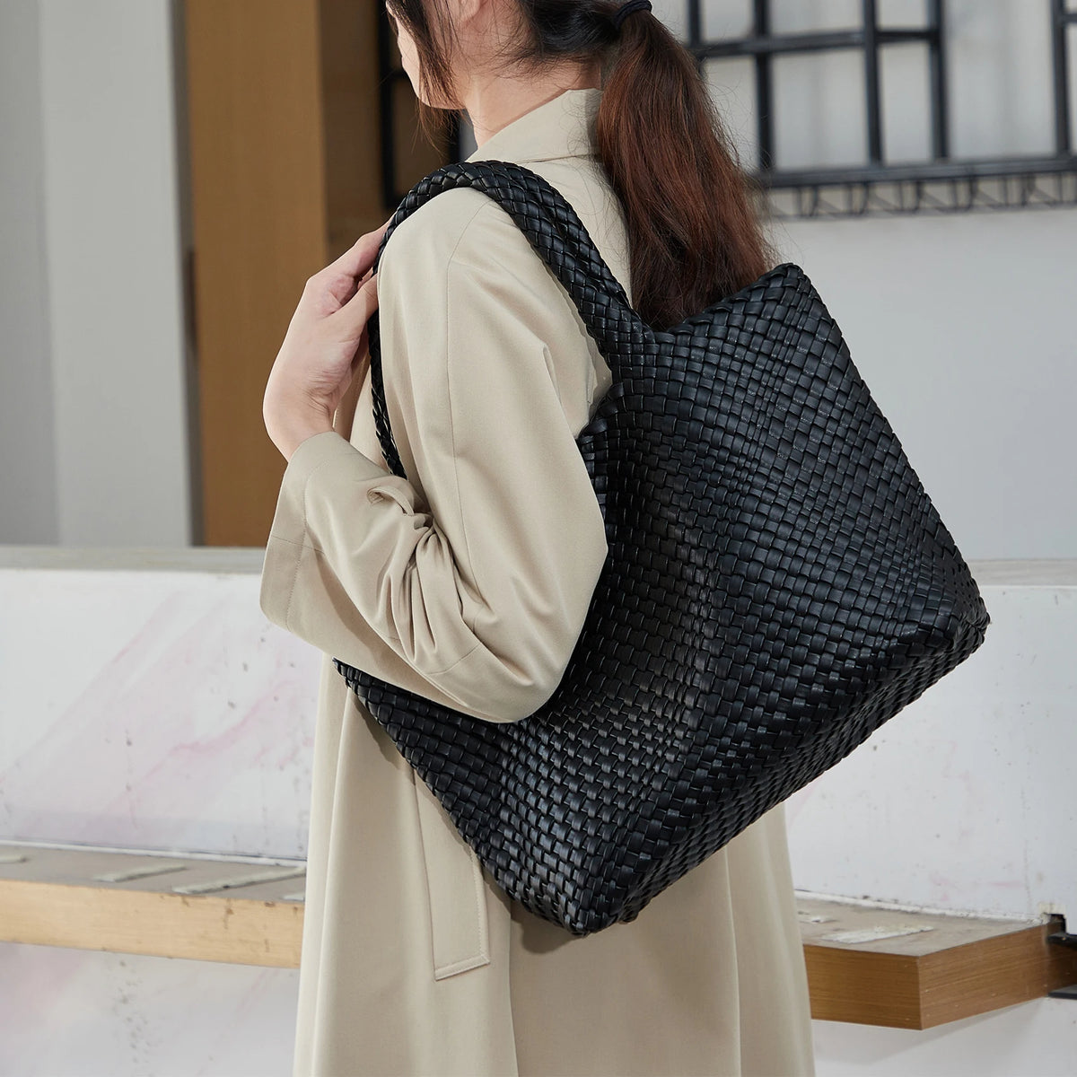 A person is carrying a black handwoven vegan leather tote bag with a textured pattern.