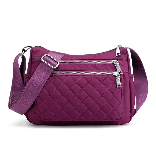 A purple quilted nylon crossbody tote bag with a silver zipper and strap.