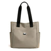 A beige nylon shoulder tote bag with black straps shown from the front.