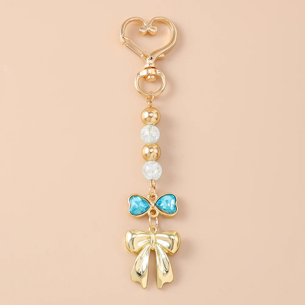 Gold pearl bow heart keychain with a blue gemstone detail