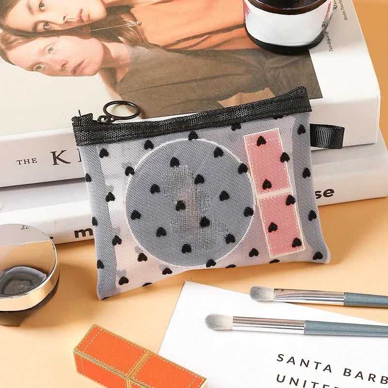 A clear mesh cosmetic storage pouch with black and pink accents rests on a wooden surface next to skincare products.