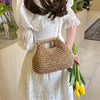 Une femme en robe blanche tient un sac à main en paille tressée et un bouquet de fleurs jaunes.