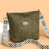 Sac à épaule et bandoulière en velours côtelé vert olive foncé avec une sangle à motif noir et blanc.
