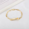 A gold-colored chain bracelet with a white and orange flower charm resting on a white background.