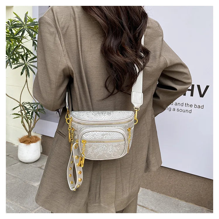 A woman is wearing a beige blazer and carrying a silver and gold rivet waist bag crossbody.