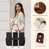 Une femme en blazer beige tient un sac fourre-tout noir et blanc avec des éléments dorés sur un fond clair.