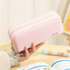 A hand holds a pink multi-layer pencil case with a special tag on a wooden surface.