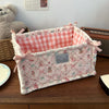 A pink and white quilted cotton storage basket with a checkered insert and pink ribbon ties sits on a wooden table.