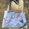 A white canvas shopping tote bag featuring a watercolor painting of pink and blue flowers in spring colors.