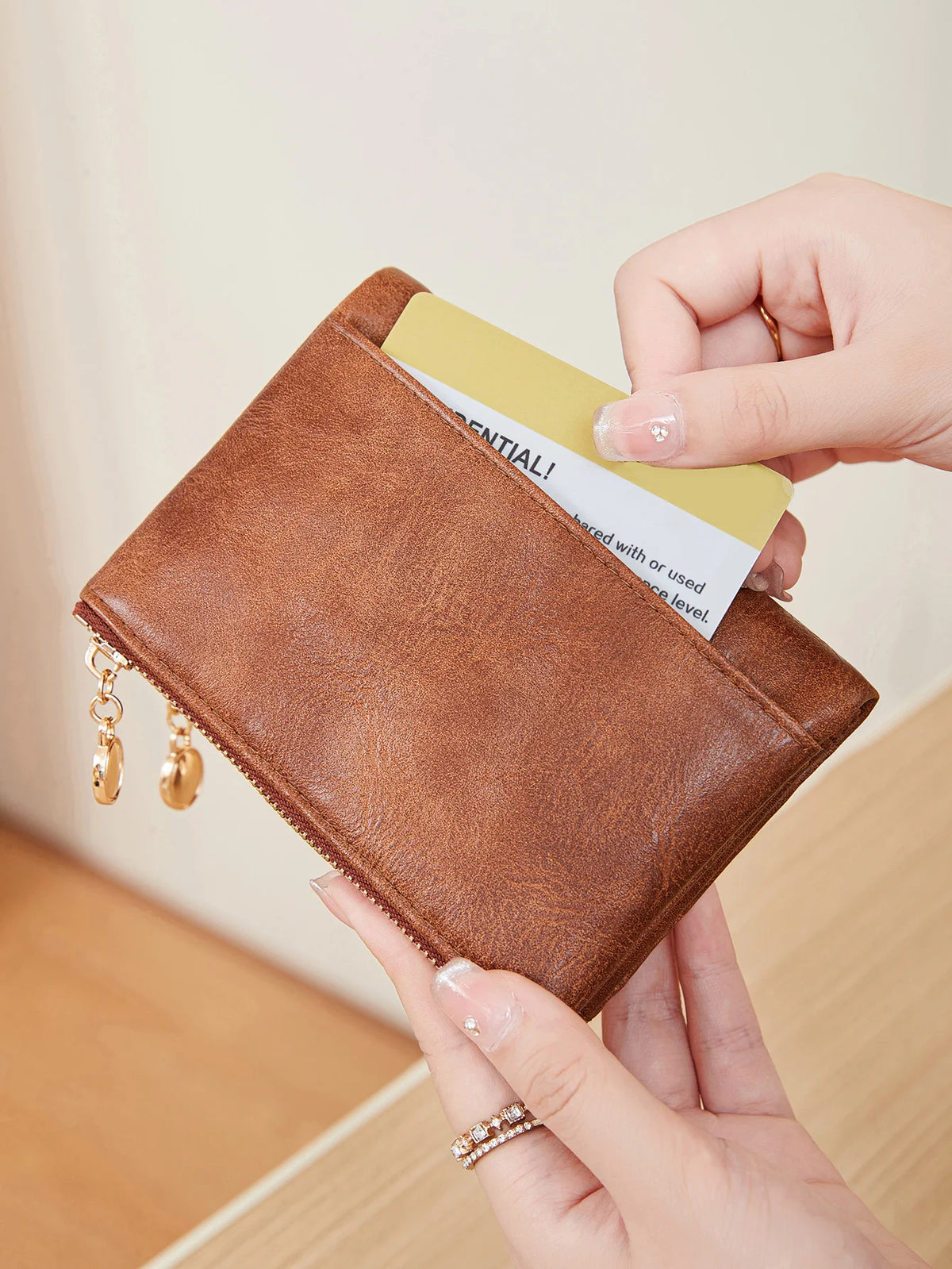 A hand holds a brown leather card holder wallet with a gold zipper and a yellow card inside.