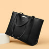 A black leather shoulder bag is shown diagonally on a light beige background.