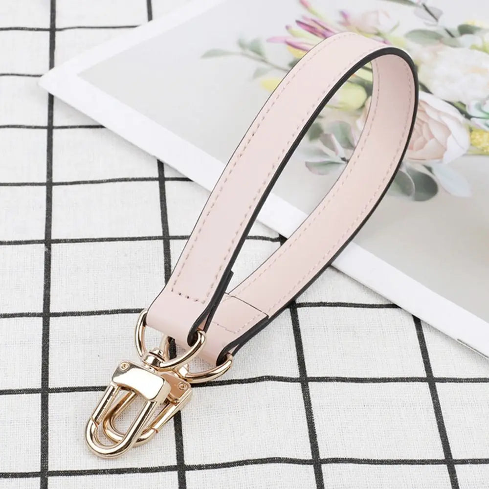 A light pink genuine leather replacement shoulder strap with a gold-toned buckle is displayed on a black and white checkered 