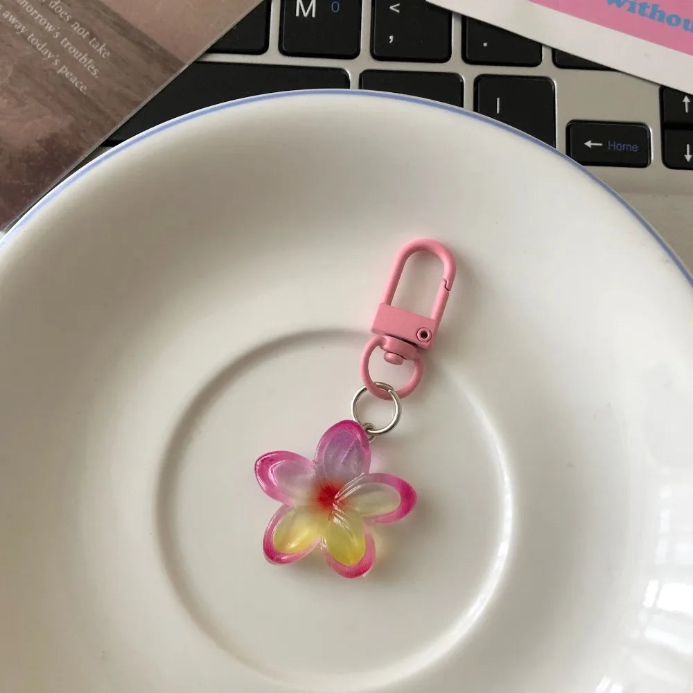 A pink resin flower keychain hanging over a white ceramic plate.