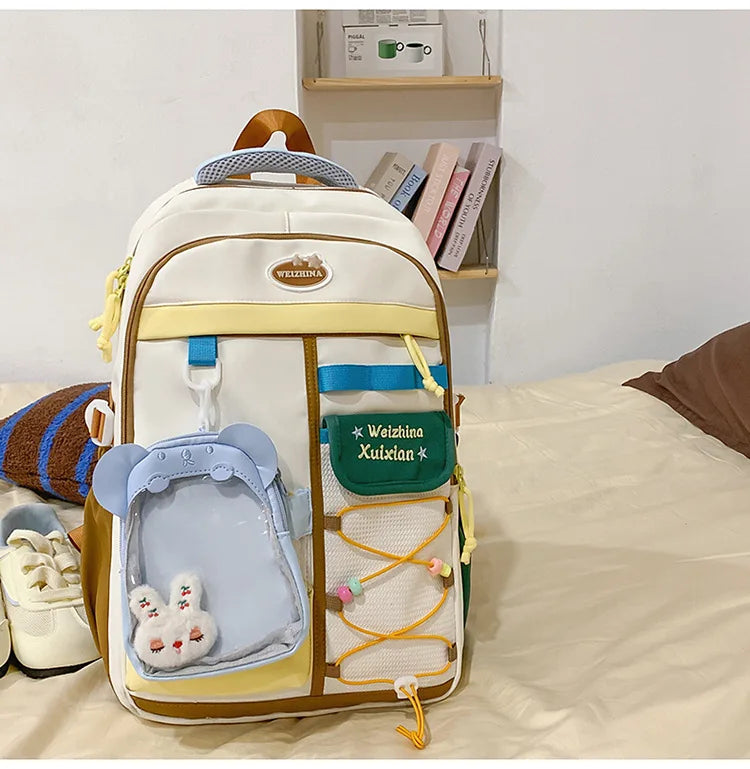 A beige and white campus backpack with blue accents and a brown strap resting on a light-colored surface.