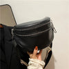 A black soft leather crossbody bag with double zippers is being held by a hand against a white background.