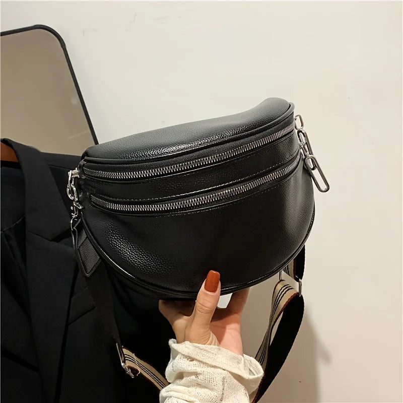 A black soft leather crossbody bag with double zippers is being held by a hand against a white background.