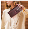A woman holds a dark burgundy genuine leather vintage clutch wallet against a light beige blazer.