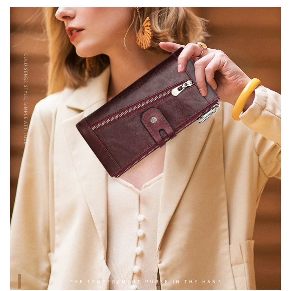 A woman holds a dark burgundy genuine leather vintage clutch wallet against a light beige blazer.