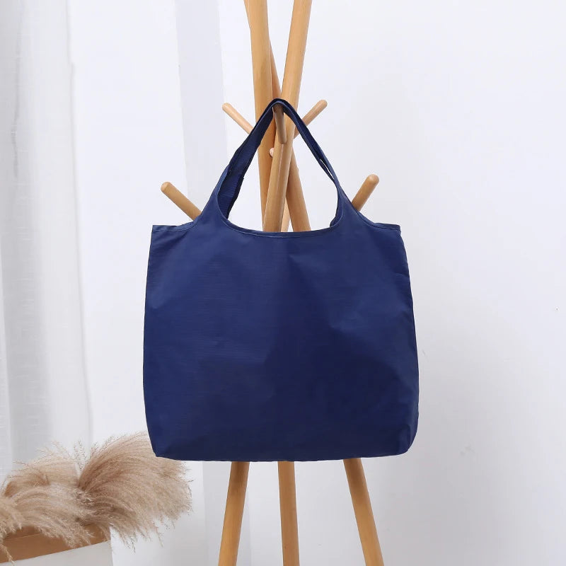 Dunkelblaue wiederverwendbare, umweltfreundliche Klapptasche hängt an einem Holzregal.