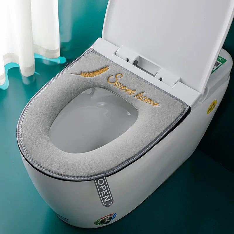 A white toilet seat cover with a soft gray cushion and gold lettering is shown open on a green surface.